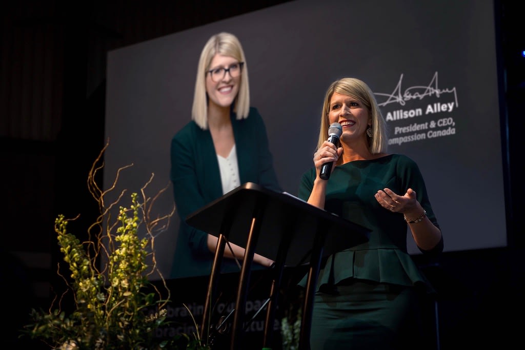 Allison holds a microphone and speaks to the guests in attendance